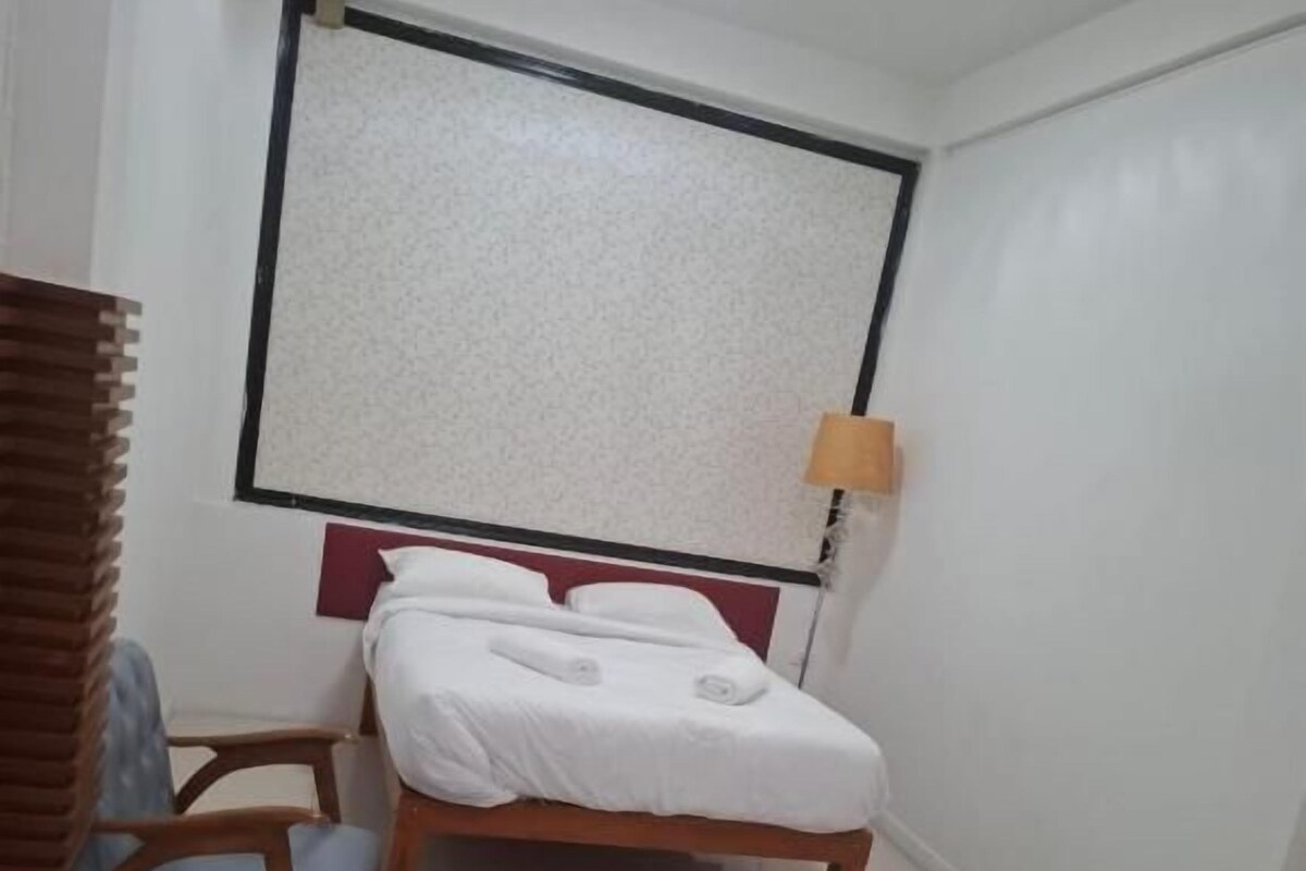 Habitación de hotel con dos camas, una ventana con persianas, un escritorio con una silla y una lámpara.