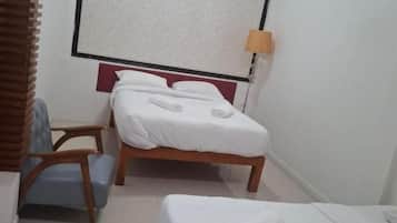 Une chambre d’hôtel avec deux lits, une fenêtre avec des stores, un bureau avec une chaise et une lampe.