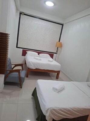 Habitación de hotel con dos camas, una ventana con persianas, un escritorio con una silla y una lámpara.