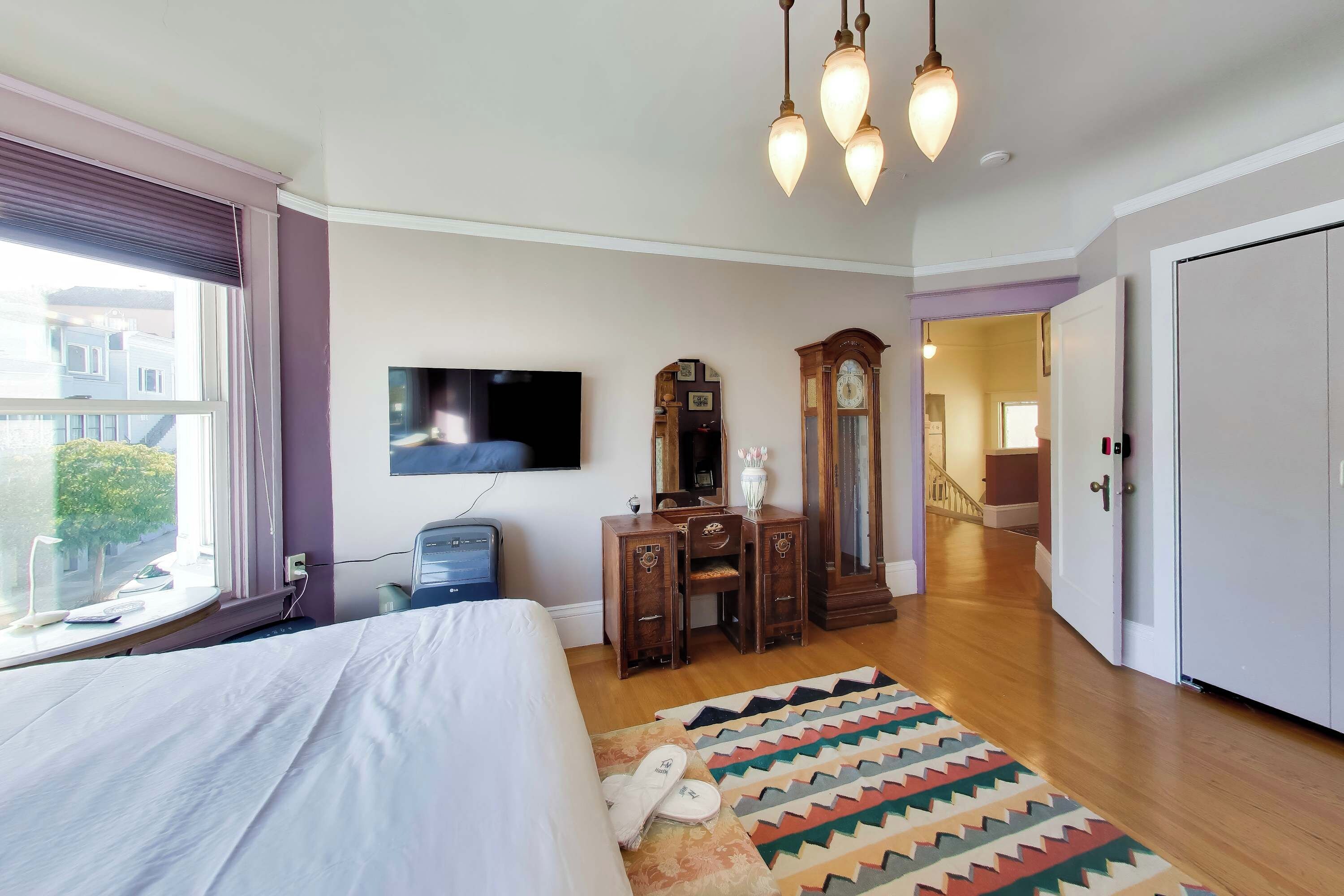 Un dormitorio con cama, televisor, cómoda, espejo y alfombra estampada.
