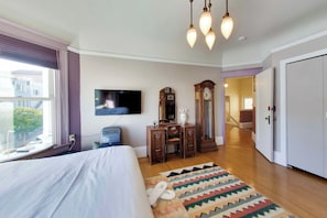 Un dormitorio con cama, televisor, cómoda, espejo y alfombra estampada.