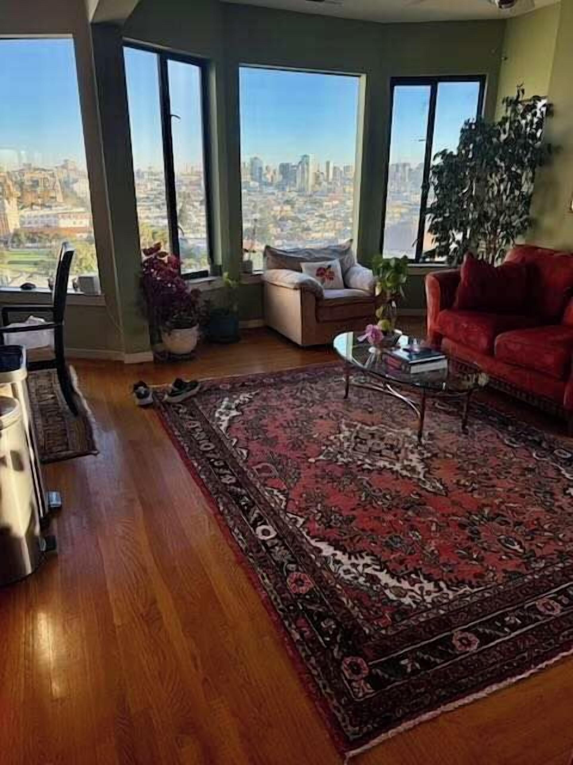 Ein geräumiges Wohnzimmer mit großem Fenster, einem roten Sofa, einem Couchtisch und einem gemusterten Teppich.