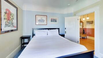 A bedroom with a bed, a nightstand, a door, and two framed pictures on the wall.