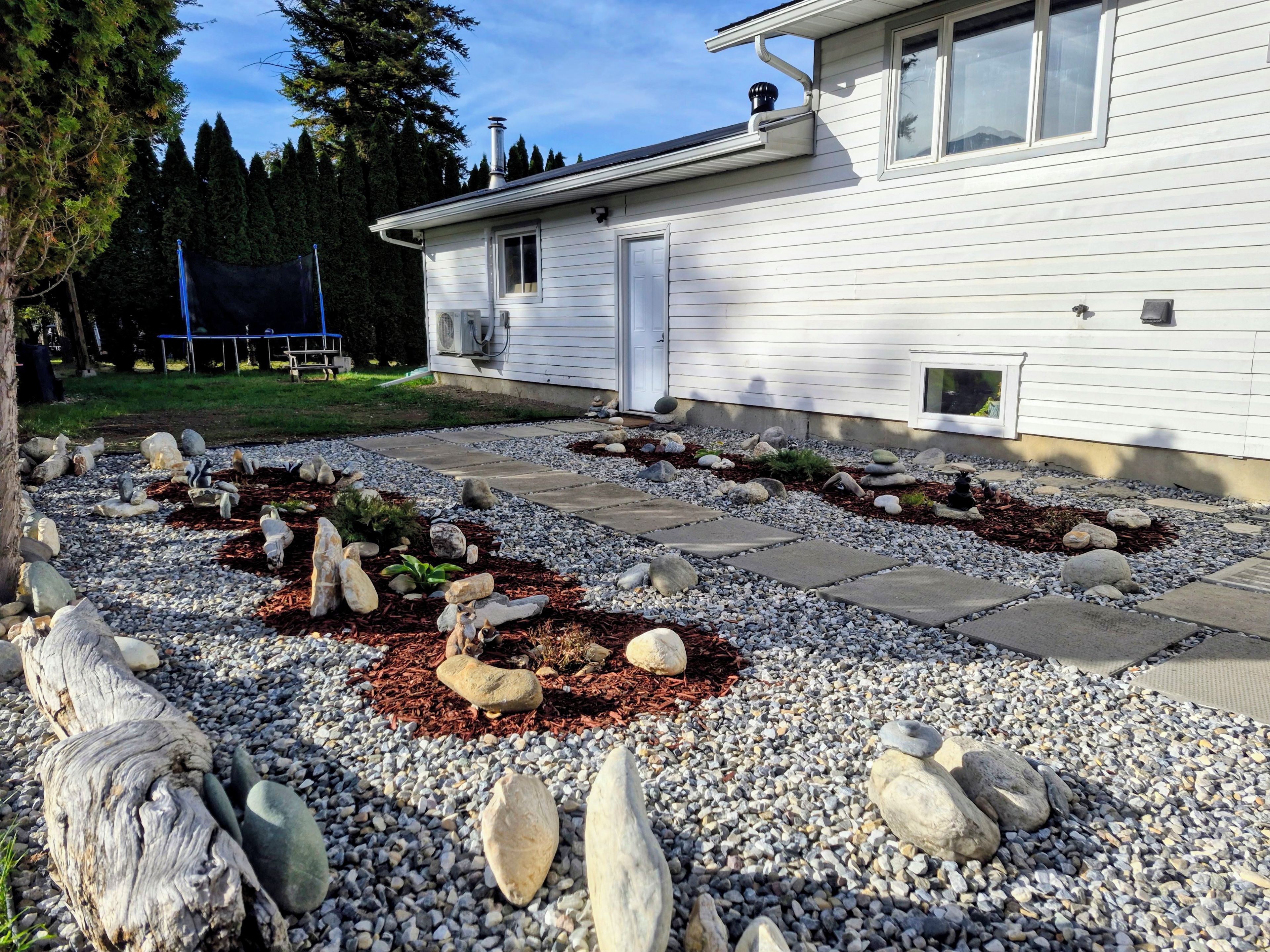 Il s’agit d’une propriété résidentielle dotée d’un chemin de gravier, d’une terrasse en bois et d’un petit jardin agrémenté de rochers et de paillis.