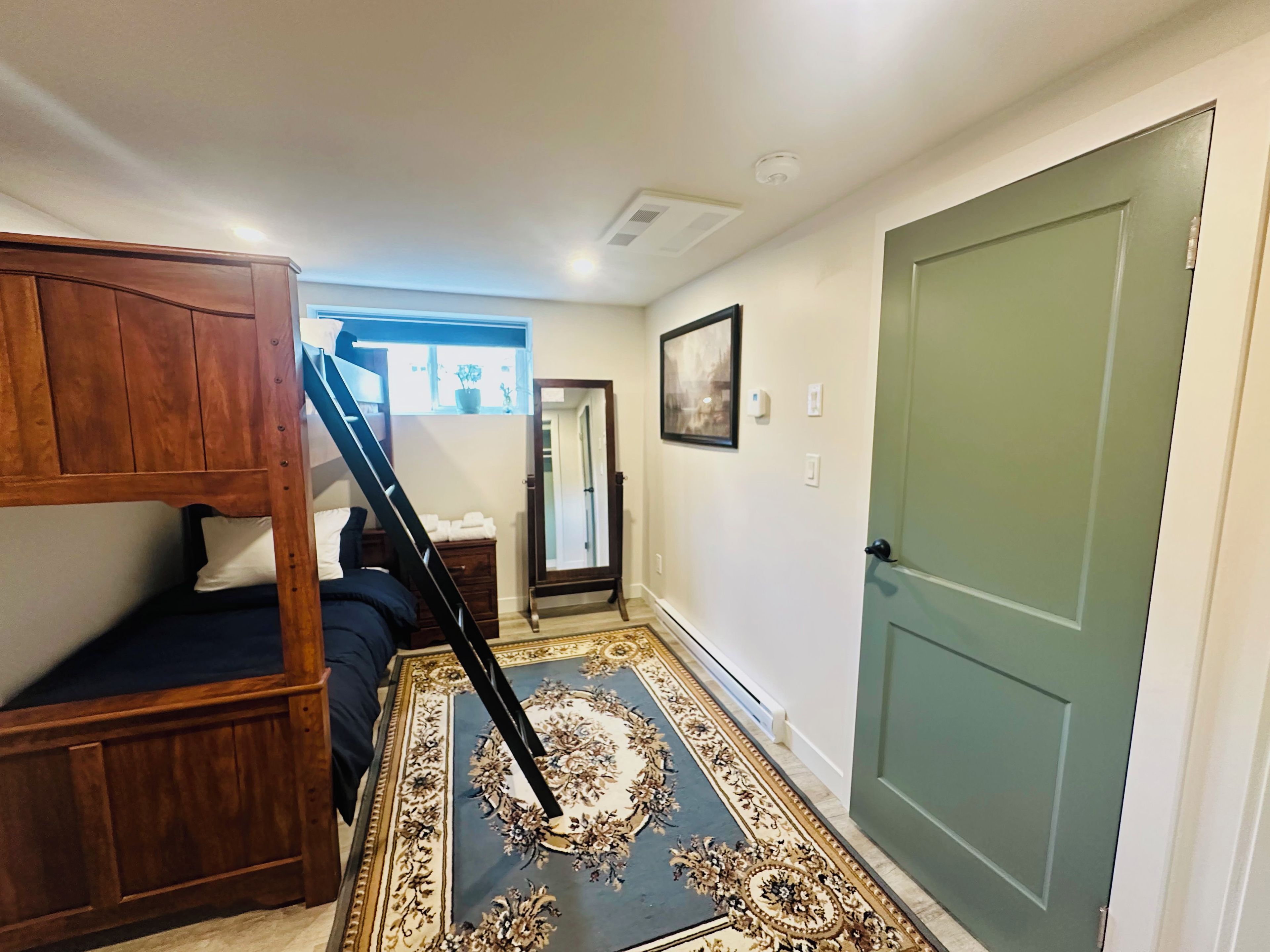 A hallway with a wooden bunk bed, a mirror, a door, and a patterned rug.