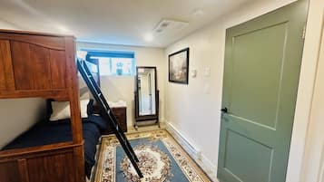 A hallway with a wooden bunk bed, a mirror, a door, and a patterned rug.