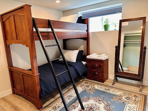A bunk bed with a ladder, a bedside table with a mirror, and a patterned rug.