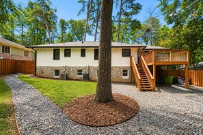 A two-story house with a stone foundation, a wooden deck, and a gravel driveway. - Cozy 1-bedroom apartment in charming Avondale Estates BRAND NEW (Avondale Estates)