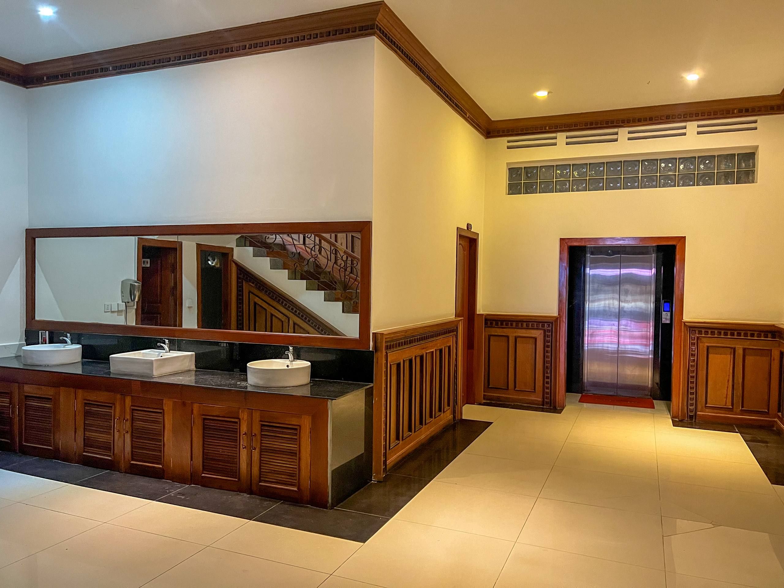 Un baño con un espejo grande, dos lavamanos, muebles de madera y piso de baldosas.