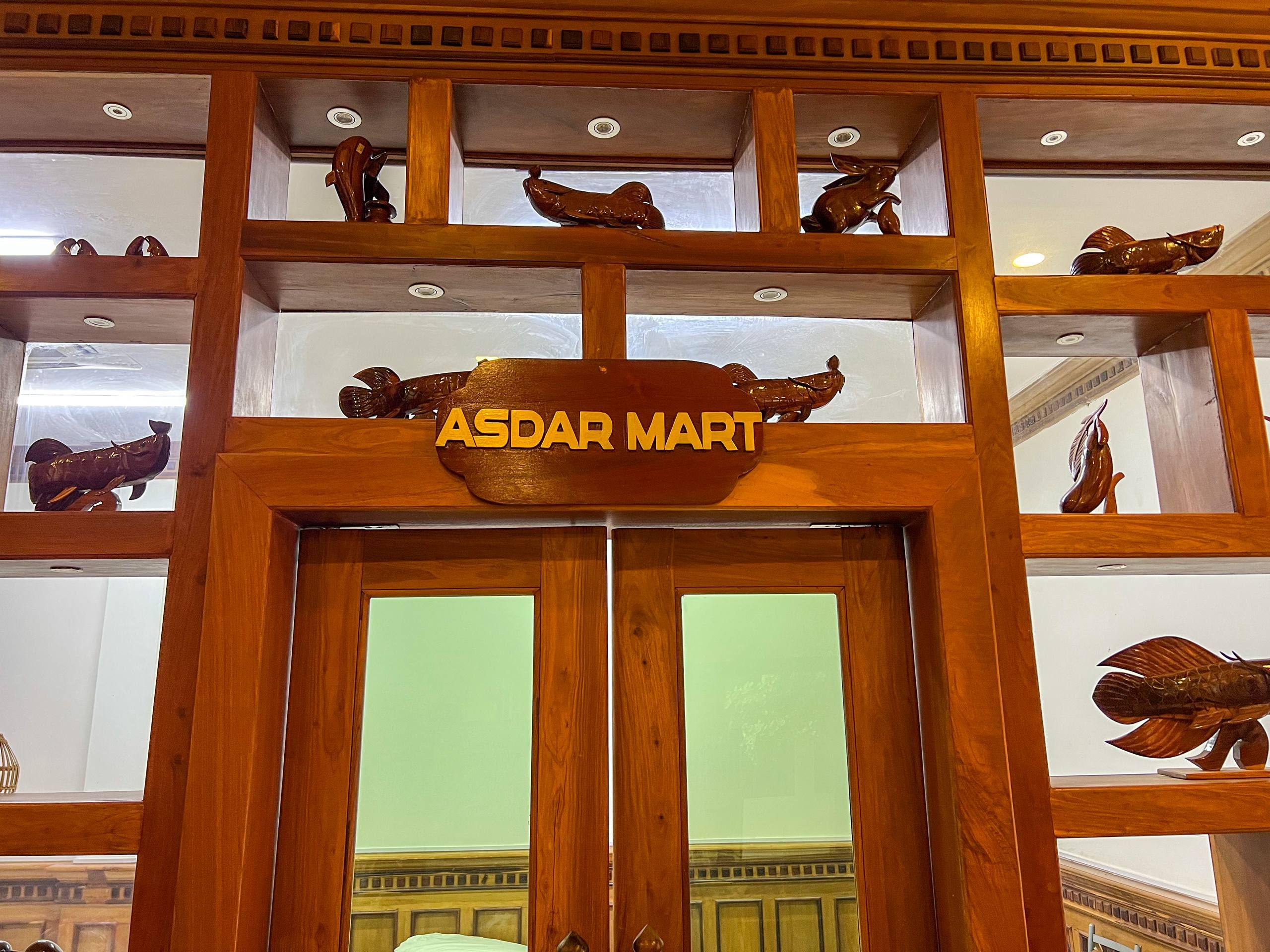 Un letrero de madera que dice 'ASDAR MART', indicando una tienda o servicio dentro de un edificio de estilo arquitectónico tradicional.