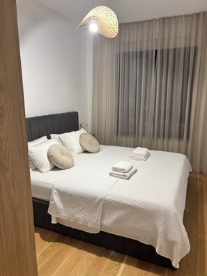 A neatly made bed with a white bedspread and pillows, a bedside lamp, and a hanging light fixture.