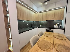 A modern kitchen with wooden cabinets, a black countertop, and a dining table with woven placemats.