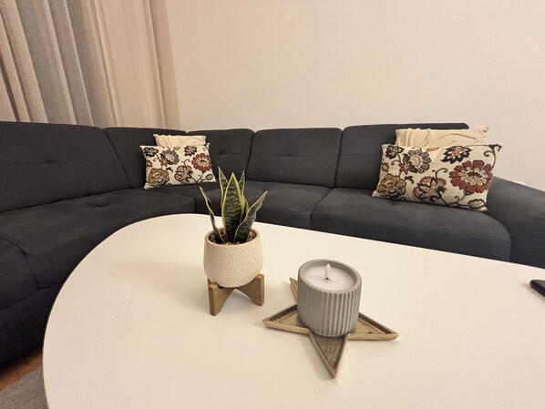 Ein modernes Wohnzimmer mit einem bogenförmigen dunkelgrauen Sofa, einem weißen Couchtisch, einer Topfpflanze und einer Kerze.