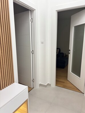 A hallway with a white door leading to a room with a dark-colored sofa and a small table.