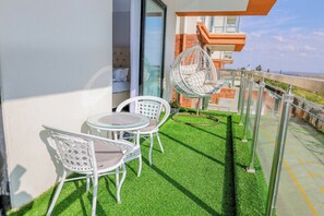 A balcony with artificial grass, white wicker furniture, and a hanging chair. - Cosy furnished apartment & family friendly with amazing animal park views (Nairobi)