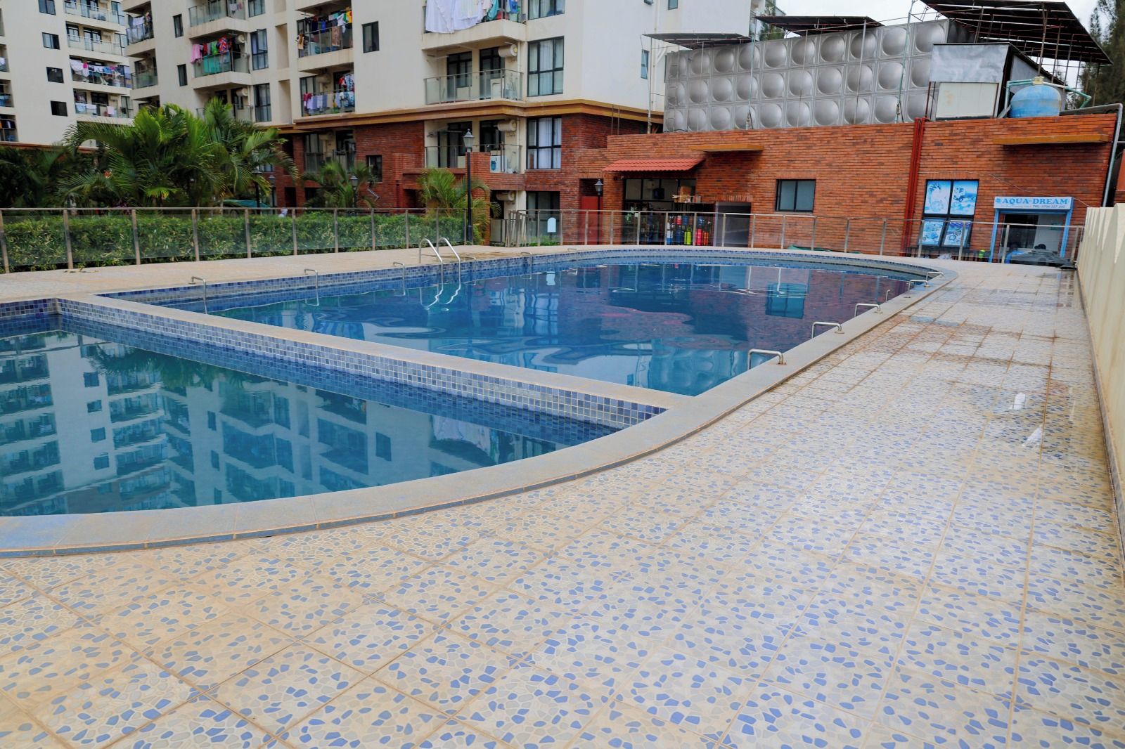 A swimming pool with a tiled deck, surrounded by residential buildings.