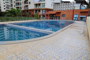 A swimming pool with a tiled deck, surrounded by residential buildings. - Cosy furnished apartment & family friendly with amazing animal park views (Nairobi)