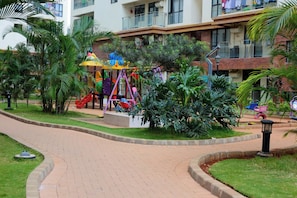 A children's playground with slides and swings, surrounded by lush greenery and a paved walkway. - Cosy furnished apartment & family friendly with amazing animal park views (Nairobi)