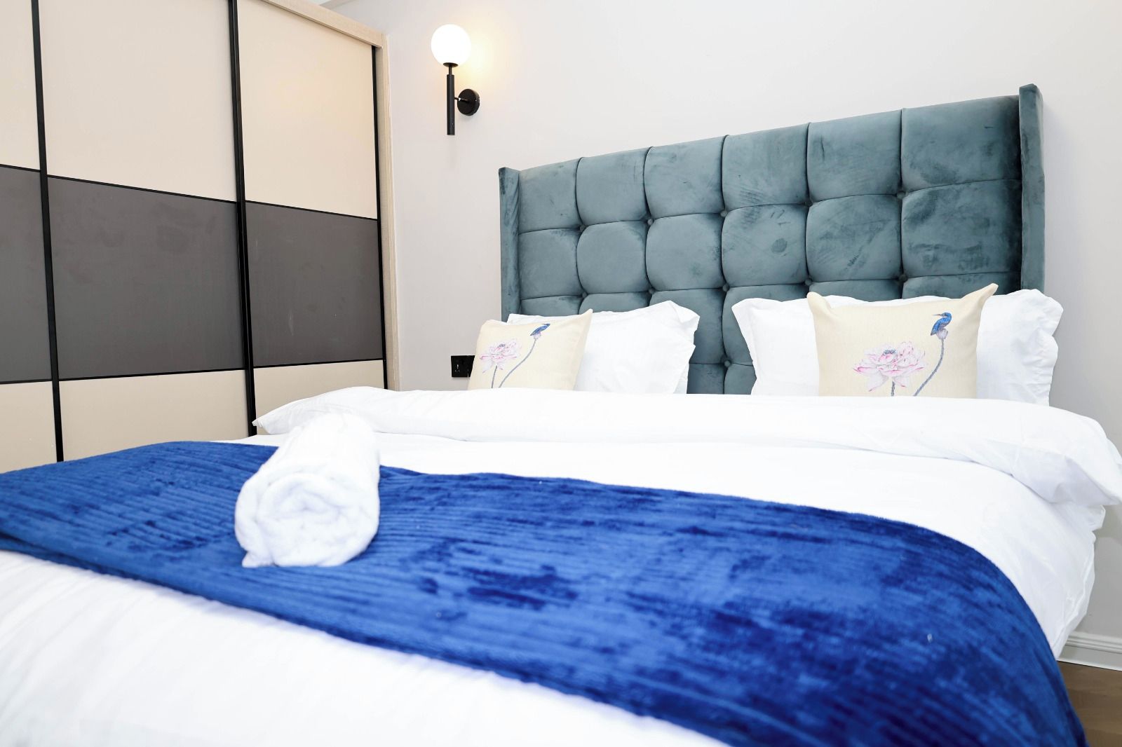 A hotel room with a bed, a headboard, and a wall-mounted light fixture.