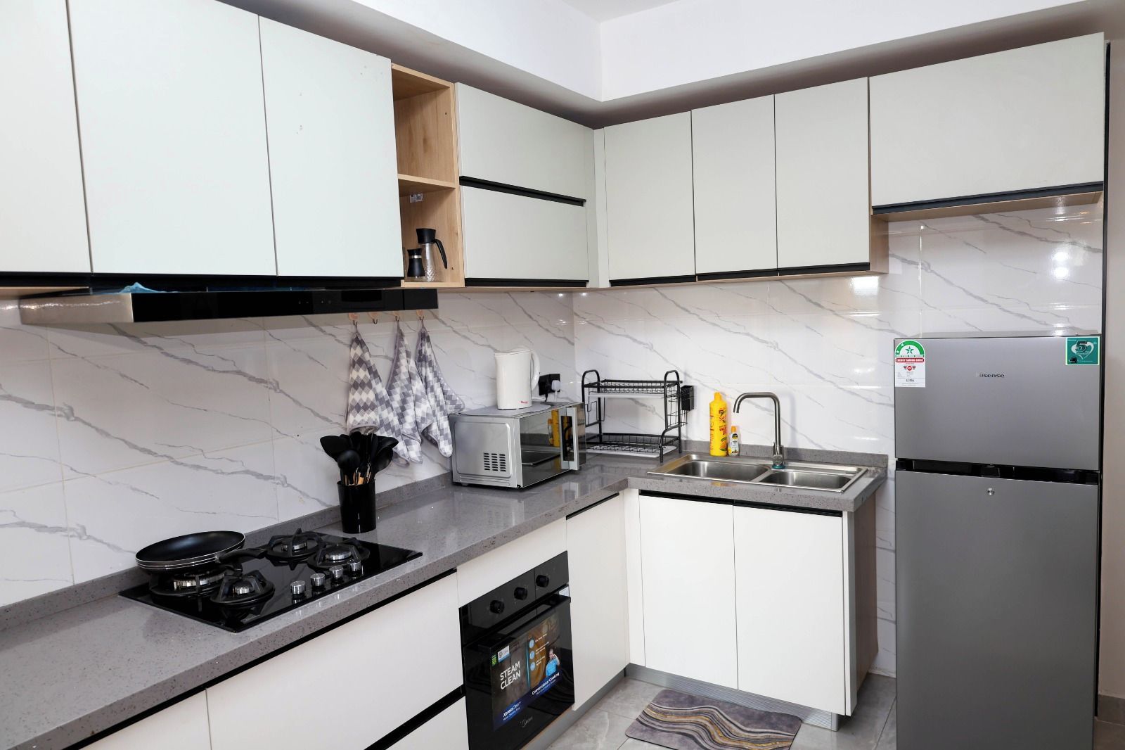 A modern kitchen with white cabinets, a stainless steel refrigerator, a built-in oven, and a gas stove.