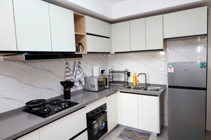 A modern kitchen with white cabinets, a stainless steel refrigerator, a built-in oven, and a gas stove. - Cosy furnished apartment & family friendly with amazing animal park views (Nairobi)
