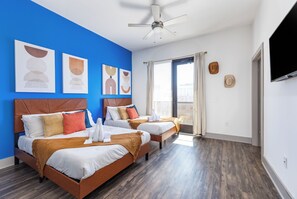 Hotellihuone, jossa on kaksi sänkyä, kattotuuletin, taideteoksia seinällä ja näkymä kaupunkiin ikkunasta.