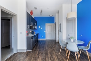 A modern kitchen with dark cabinets, a blue accent wall, and a dining area with a round table and chairs. - 5 Minutes to Downtown + Pool + Fitness Gym + Free Parking (Nashville)