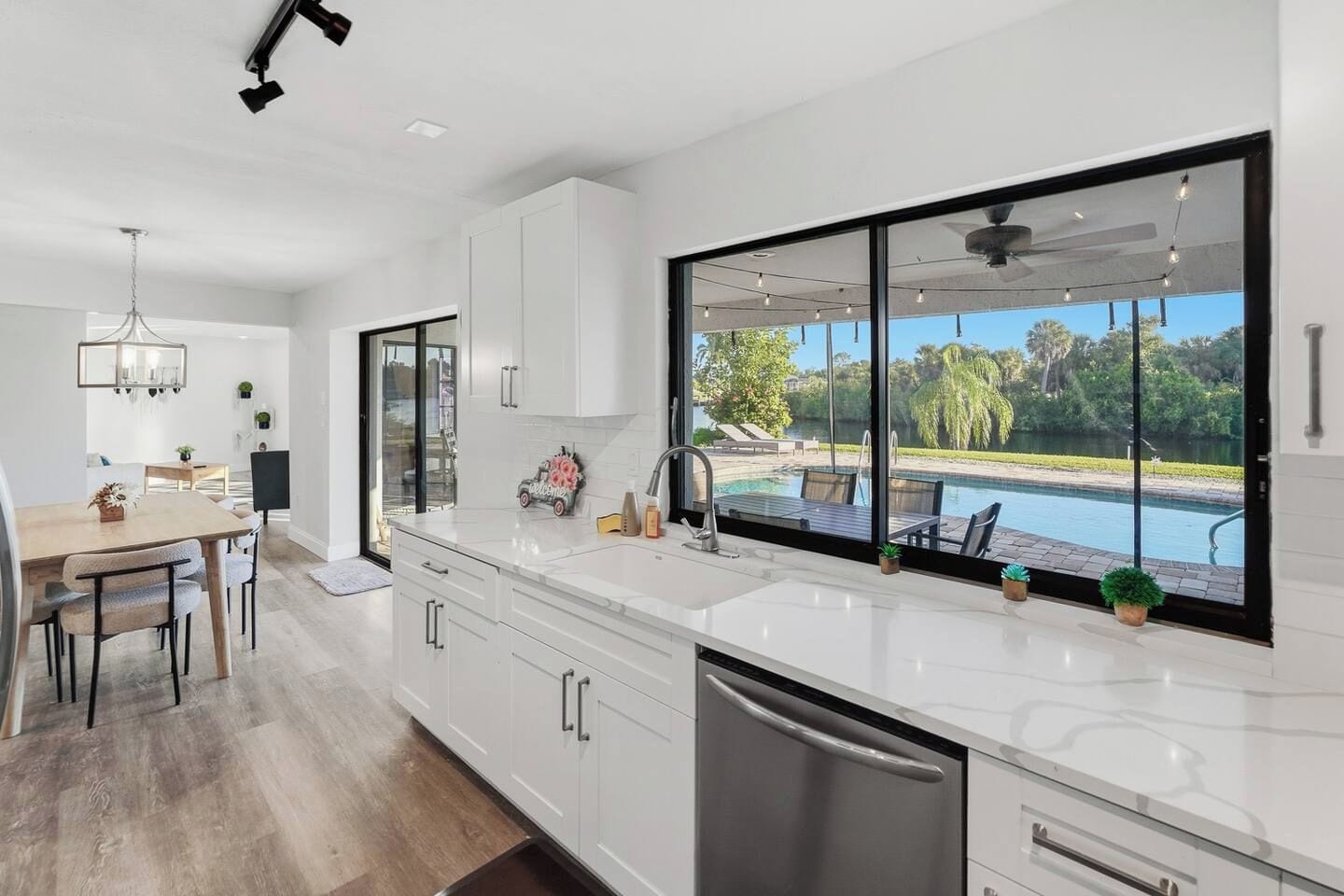 A modern kitchen with a large window overlooking a swimming pool and garden.