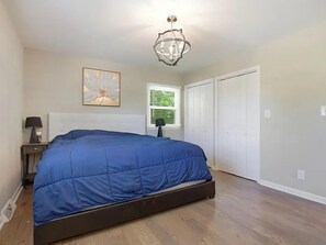 Ein Schlafzimmer mit einem Bett, einem Nachttisch, einer Lampe, einem Fenster mit Jalousien und einer Tür.