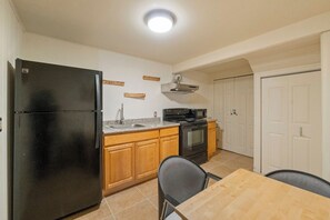 A compact kitchen with a black refrigerator, wooden cabinets, a sink, a stove, and a dining table with two chairs. - Queen Anne Home, Space Needle Walk + Parking (Seattle)