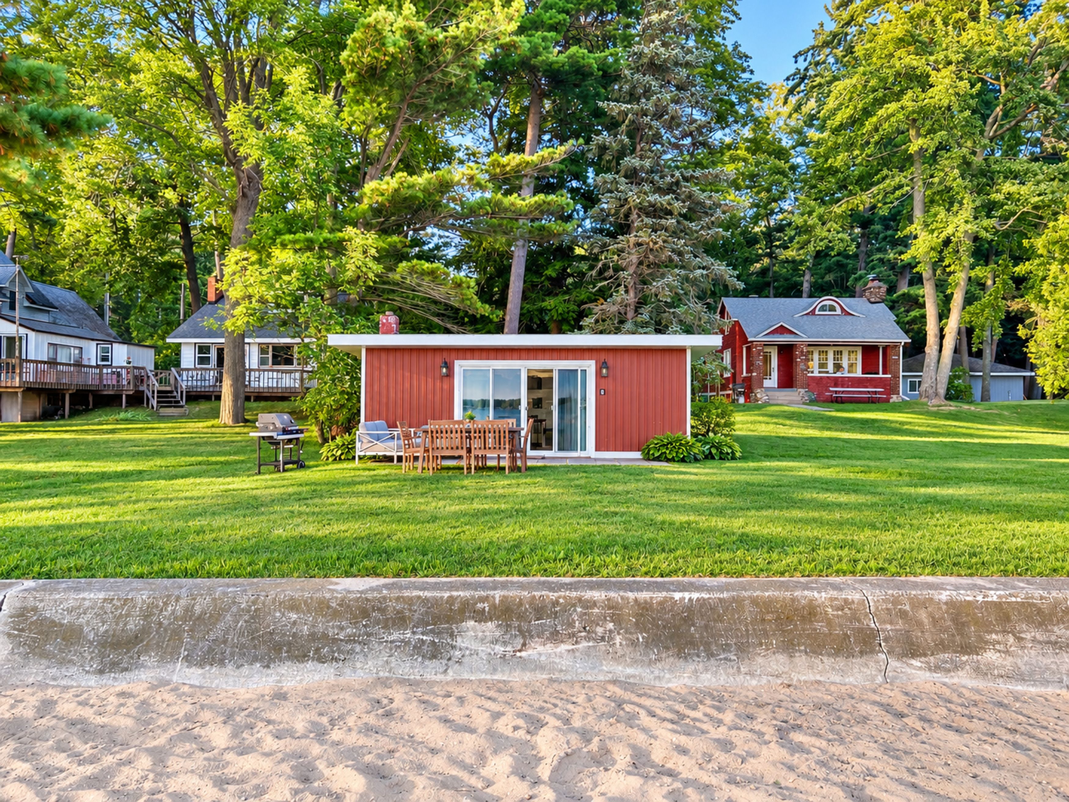 Ett bostadsområde med ett litet rött hus, ett större hus med en veranda och en gräsig trädgård.