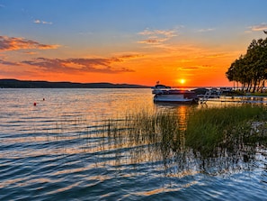 Ein ruhiger See bei Sonnenuntergang mit anlegenden Booten, umgeben von Bäumen und einem klaren Himmel.