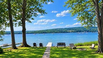 A lakeside view with a pathway leading to a dock, surrounded by trees and chairs.