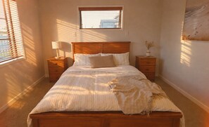 Un dormitorio con cama, mesitas de noche, una ventana y una obra de arte colgada en la pared.