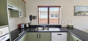 Eine Küche mit Backofen, Toaster, Wasserkocher, Spüle und einem Fenster mit Jalousien.
