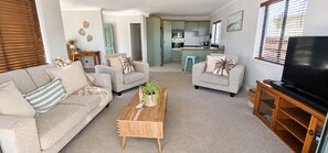 A living room with a sofa, armchairs, a coffee table, and a TV stand. - OCEAN BREEZE ESCAPE
Four Minute Walk To Beach, Town & Clubs (Whangamatā)