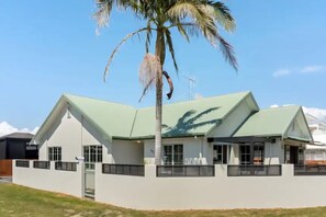 A modern building with a green roof, large windows, and a palm tree in the foreground. - OCEAN BREEZE ESCAPE
Four Minute Walk To Beach, Town & Clubs (Whangamatā)