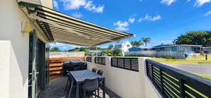 An outdoor patio with a table and chairs, a covered area, and a view of neighboring houses. - OCEAN BREEZE ESCAPE
Four Minute Walk To Beach, Town & Clubs (Whangamatā)