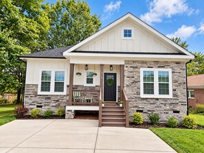 A two-story house with a stone facade, a front porch with a bench, and a small staircase leading to the entrance. - Peak on First I Modern Bungalow Near Downtown Apex (Apex)