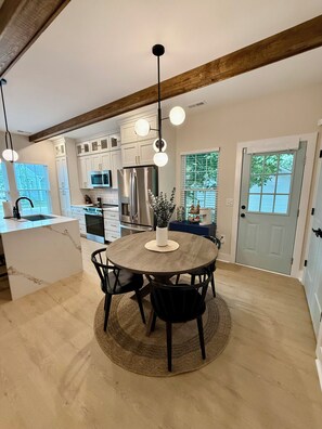 A modern kitchen with white cabinets, a central island, and a dining area with a round table and chairs. - Peak on First I Modern Bungalow Near Downtown Apex (Apex)