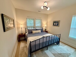 A bedroom with a bed, two bedside tables, a wall-mounted lamp, and a ceiling light fixture. - Peak on First I Modern Bungalow Near Downtown Apex (Apex)