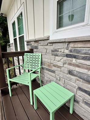 A porch with a green chair and a matching table, a stone wall, and a window with a view of the outdoors. - Peak on First I Modern Bungalow Near Downtown Apex (Apex)