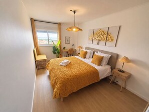 A hotel room with a bed, bedside tables, a desk, a chair, a window with curtains, a plant, and a view of the outside. - Lisbon • Spacious 2BR • Balcony • Elevator • WiFi (Lisboa)