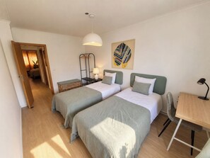 Ein Hotelzimmer mit zwei Betten, einem Schreibtisch, einem Stuhl, einer Lampe und einem Bild an der Wand.