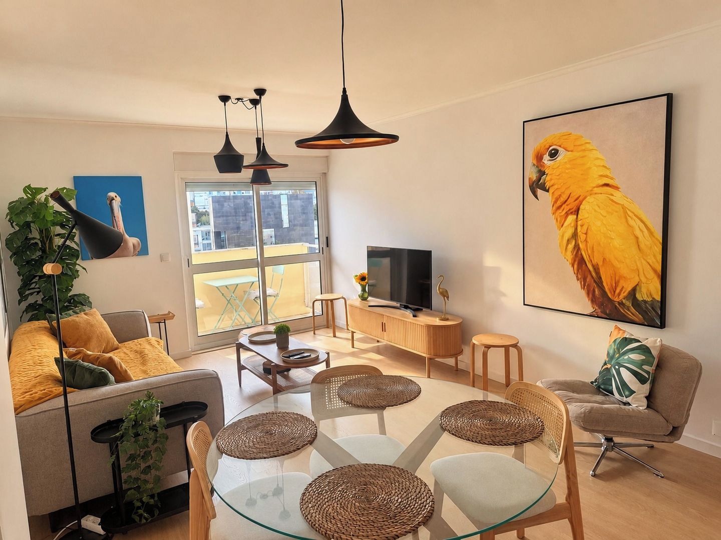 A modern living room with a glass dining table, comfortable seating, a large window, and a television.