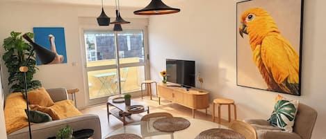 A modern living room with a glass dining table, comfortable seating, a large window, and a television.