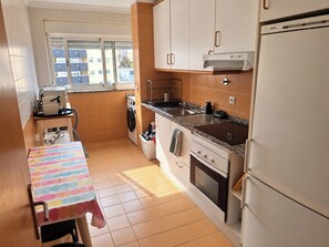 Eine kompakte Küche mit Waschmaschine, einem Tisch mit bunten Tischdecken und einem Kühlschrank.