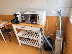 Een kleine kitchenette met een magnetron, een koffiezetapparaat en een stofzuiger.