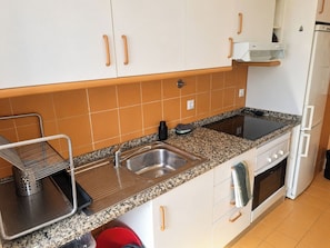 Een keuken met witte kastjes, een granieten aanrecht, een spoelbak, een fornuis en een koelkast.