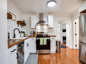 A modern kitchen with white cabinetry, stainless steel appliances, and a wooden countertop. - Costy Stay | 8 minutes to Downtown & Broadway | Free Parking (Nashville)